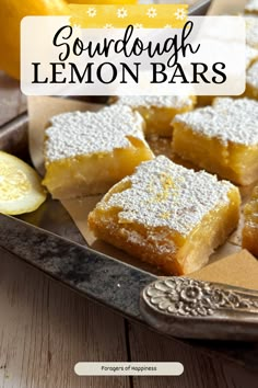 lemon bars with powdered sugar on top in a metal tray next to sliced lemons