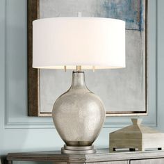 a silver table lamp sitting on top of a wooden dresser next to a framed painting