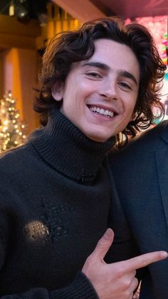 two young men standing next to each other in front of a building with christmas lights