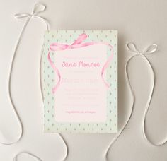 a pink and green wedding card with a bow on it's front, sitting on a white surface