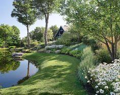 a lush green field with flowers and trees next to a pond in the middle of it