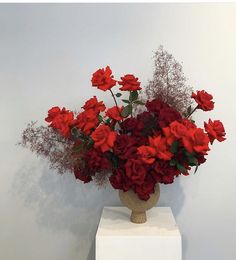 a vase filled with red flowers on top of a white pedestal