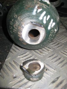 an old green vase sitting on top of a metal grate with holes in it