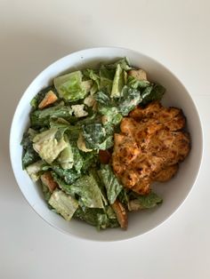 a white bowl filled with lettuce and chicken on top of a white table