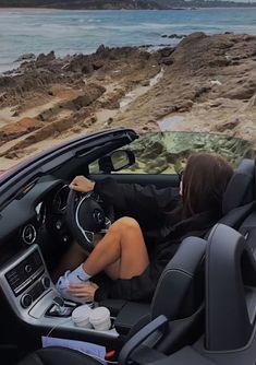 a woman sitting in the driver's seat of a car next to the ocean