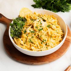 a white bowl filled with pasta and parsley on top of a wooden cutting board