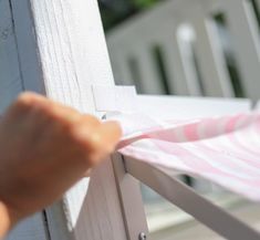 someone is pulling the pink and white striped fabric off of a wooden porch chair that's outside