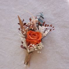 a boutonniere with an orange rose on it sitting on a white cloth