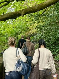 three people walking up a wooden path in the woods with bags on their backs and one person carrying a blue handbag