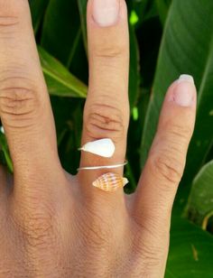 a person's hand with a ring on it and some leaves in the background