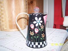 a black and white coffee pot with flowers painted on the side sitting on a table