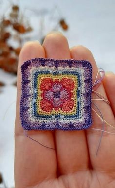 a hand holding a small square with a flower in the center and thread on it