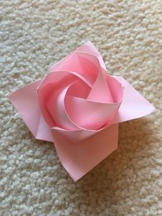 an origami flower on the floor with white carpet in the background and light pink