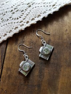 pair of silver earrings with green and white flowers on them sitting on top of a wooden table