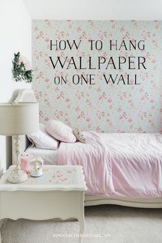 a bedroom with a pink bed and floral wallpaper on the wall behind it is a white table lamp