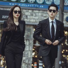 two people in suits and sunglasses walking down the street