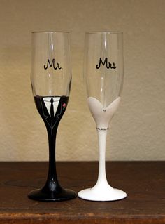 two wine glasses with names on them sitting on top of a wooden table next to each other