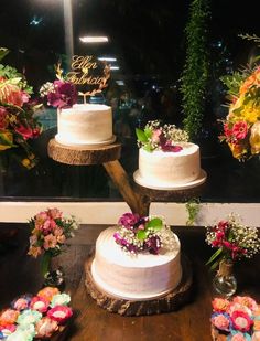 three tiered wedding cake displayed in front of a window with flowers and greenery