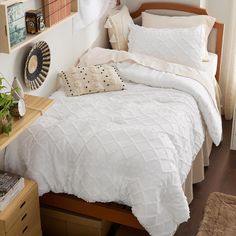 a bed with white comforter and pillows in a bedroom next to a wooden dresser