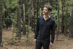 a man standing in the middle of a forest looking off into the distance with trees behind him