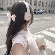 a woman with headphones on walking down the street holding a coffee cup and a cell phone