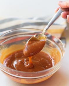 a spoon full of peanut butter and caramel sauce in a glass bowl on a table