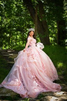 a woman in a pink dress is posing for the camera with trees and rocks behind her