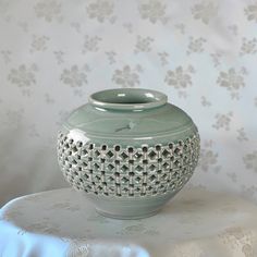 a green vase sitting on top of a white tablecloth covered table next to a floral wallpaper