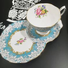 an antique tea cup and saucer with floral designs on the rim, sitting on a black table