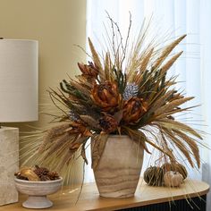 an arrangement of dried flowers in a vase on a table next to a lamp and other items