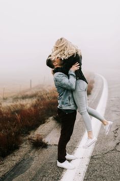 a man and woman hugging on the side of an empty road in foggy weather