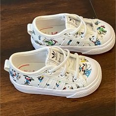 Pay Tribute To Your Favorite Cartoon Character With The Nizza Goofy White Shoes From Adidas X Disney! The Iconic Dog Appears Throughout These Shoes Dressed For A Variety Of Sports, Including Baseball, Skateboarding, Karate And Surfing, Spilling A Bunch Of Silly Style Into These Stunning Sneakers. A Comfortable Eva Insole And Cushioned Footbed Mean Your Feet Will Be Feeling Great All Day Long, Making The Nizza Goofy Shoes Perfect For Any Collection. Cartoon Character Print Low-top Sneakers, Cartoon Print Sneakers With Round Toe, Fun Low-top Sneakers With Cartoon Print, Fun Sneakers With Character Print And Round Toe, White Low-top Sneakers With Cartoon Print, Fun Cartoon Print Sneakers With Round Toe, Disney Character Print Sneakers With Round Toe, Playful Cartoon Print Sneakers With Round Toe, Playful Cartoon Print Round Toe Sneakers