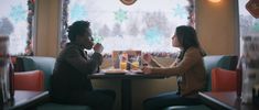 two people sitting at a table in a restaurant eating food and drinking orange juices