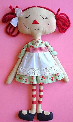 a doll with red hair wearing a white dress and striped socks, on a pink background