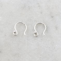 two silver ear hooks on a white marble surface with the end of one hook in the middle