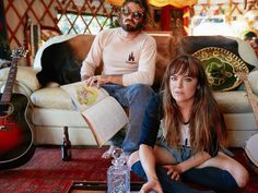 two people sitting on a couch in a living room next to each other with guitars