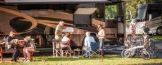 people sitting at tables in front of an rv with bikes parked next to the road