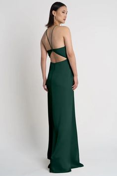 the back of a woman wearing a dark green evening gown with cut out shoulders and straps