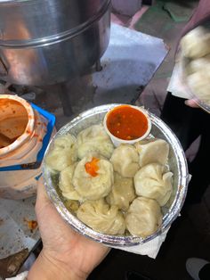 a person holding a tin foil container filled with dumplings and sauce on top of it