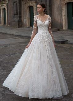 a woman in a white wedding dress standing on the street with an old building behind her