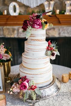 a three tiered cake with flowers on top sits on a table next to candles