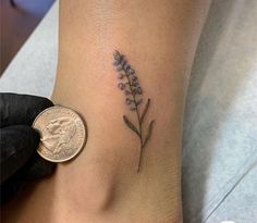 a small lavender flower tattoo on the right side of the ankle by a dime penny