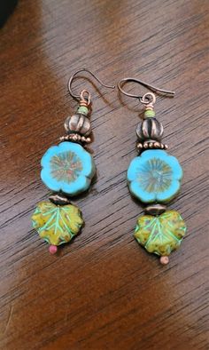 two dangle earrings with blue and green designs on them sitting on a wooden table