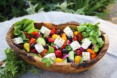 a wooden bowl filled with vegetables and feta cheese on top of a stone table