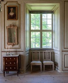 two chairs and a table in front of a window with a painting on the wall