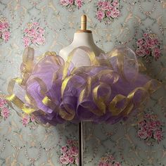 a mannequin with purple and gold tulle on it's head stands in front of a floral wallpaper