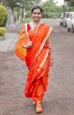 a woman in an orange sari is walking down the street with her hand on her hip