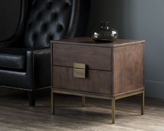 a black chair next to a wooden table with a drawer on it and a vase sitting on top of it