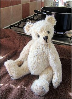 a white teddy bear sitting on top of a brown towel next to a stove burner