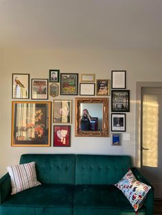 a green couch sitting in front of a wall filled with pictures and framed photos on it